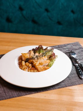 Kızarmış tavuk göğsü ile patates, marul ve biberiye dalı bıçak, çatal ve gri peçete ile beyaz tabakta servis