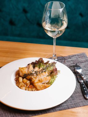 Kızarmış tavuk göğsü ile patates, marul ve biberiye şube hizmet beyaz plaka üzerinde bıçak, çatal, gri peçete ve beyaz şarap ile