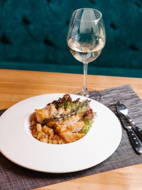 Kızarmış tavuk göğsü ile patates, marul ve biberiye şube hizmet beyaz plaka üzerinde bıçak, çatal, gri peçete ve beyaz şarap ile