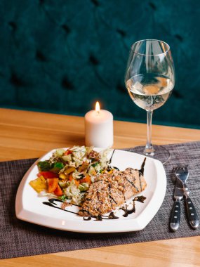 Ekmekli tavuk göğsü kıyılmış ceviz ve domates, biber, marul, salatalık ile çatal, bıçak, peçete, beyaz şarap ve mum arka plan üzerinde beyaz tabakta servis balsamik soslu salata ile