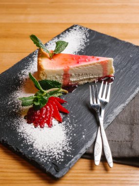 Cheesecake taş dilimlenmiş çilek, nane yaprakları ve çatal ile tabakta meyve şurubu ile
