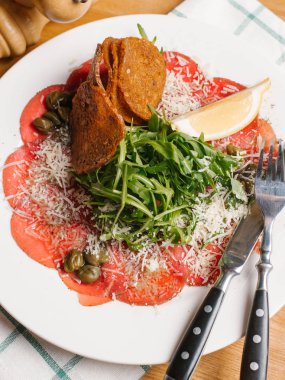 Biberli ekmek tost ile dilimlenmiş, roka, Kapari ve limon dilim rendelenmiş parmesan ile dekore edilmiş bıçak, çatal, karabiber öğütücüsü ve Damalı peçete beyaz tabakta