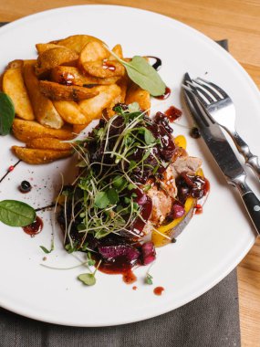 Karamelize tatlı soğan, kabak, berry sos ve bezelye ile kavrulmuş et beyaz peçete, bıçak ve çatal ile tabakta derin kızarmış patates ile lahanası