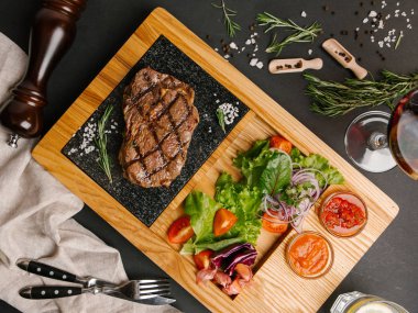 Üstten görünüm taze domates, marul, tatlı soğan ile ızgara sığır eti biftek ketçap ve barbekü sosu bıçak, çatal ve içecekler ile ahşap yemek servis
