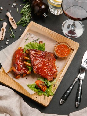Pişmiş domuz kaburga ile domates, marul ve Barbekü parşömen kağıt, limonata, şarap, bıçak ve çatal ile ahşap yemek üzerine sos