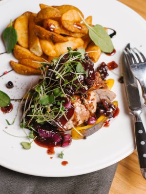 Karamelize tatlı soğan, kabak, berry sos ve bezelye ile kavrulmuş et beyaz peçete, bıçak ve çatal ile tabakta derin kızarmış patates ile lahanası