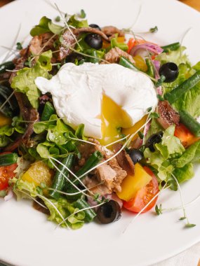 Füme yılan balığı, tatlı biber, domates, zeytin, salata, tatlı soğan, yeşil fasulye ve bezelye lahanası salatası haşlanmış yumurta ile beyaz tabakta servis