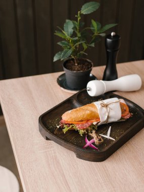 Baget salam, jambon, domates ve marul ile tatlı soğan ve karabiber, tuz değirmeni, karabiber öğütücüsü ve arka plan üzerinde vazo ile ahşap yemek servis