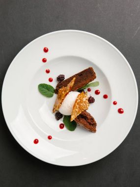 Çikolatalı pasta, dondurma ve fıstık ile karamel ile şık tatlı meyve şurubu, çilek ve nane yaprakları ile süslenmiş beyaz tabakta servis