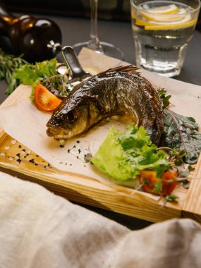 Domates balıkla pişmiş, parşömen kağıt, limonata ve şarap ile ahşap yemek marul, otlar ve limon basın servis