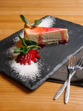 Cheesecake taş dilimlenmiş çilek, nane yaprakları ve çatal ile tabakta meyve şurubu ile