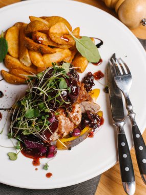 Kavrulmuş et ile tatlı soğan, kabak, berry soslu karamelize ve bezelye lahanası beyaz tabakta peçete, çatal, bıçak ve karabiber değirmeni ile derin kızarmış patates ile