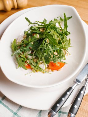 Tabak, çatal, bıçak, karabiber öğütücüsü ve peçete ahşap masa üzerinde beyaz kase dilimlenmiş domates ve çam fıstığı roka, kızarmış yumurta closeup hizmet