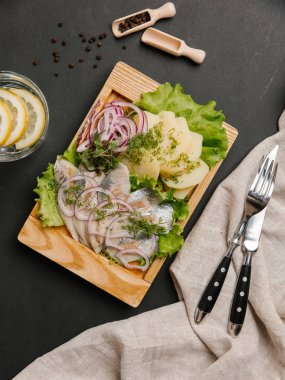 Ringa balığı, tatlı soğan, yeşillik ve marul limonata, çatal ve bıçak ile ahşap yemek üzerine haşlanmış patates hizmet