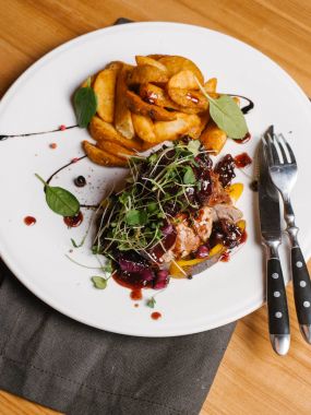 Karamelize tatlı soğan, kabak, berry sos ve bezelye ile kavrulmuş et beyaz peçete, bıçak ve çatal ile tabakta derin kızarmış patates ile lahanası