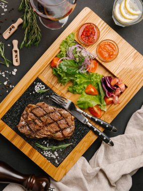 Üstten Görünüm taze domates, marul, tatlı soğan ile ızgara sığır eti biftek ketçap ve barbekü sosu, çatal, bıçak, limonata ve şarap ile ahşap yemek servis