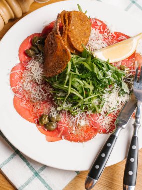 Biberli ekmek tost ile dilimlenmiş, roka, Kapari ve limon dilim rendelenmiş parmesan ile dekore edilmiş bıçak, çatal, karabiber öğütücüsü ve Damalı peçete beyaz tabakta