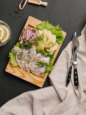 Haşlanmış patates ile ringa balığı, tatlı soğan, yeşillik ve marul limonata, çatal ve bıçak ile ahşap yemek üzerine servis Üstten Görünüm