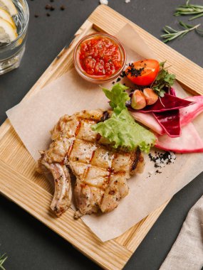 Izgara domuz karnabahar, marul, domates, sarımsak ve ahşap tabak üzerinde parşömen kağıt ve limonata eşliğinde barbekü sosu ile