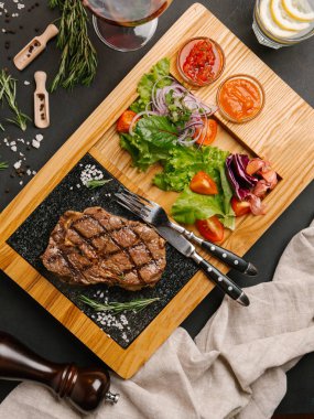 Üstten Görünüm taze domates, marul, tatlı soğan ile ızgara sığır eti biftek ketçap ve barbekü sosu, çatal, bıçak, limonata ve şarap ile ahşap yemek servis