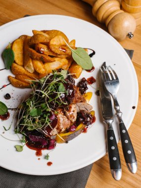 Kavrulmuş et ile tatlı soğan, kabak, berry soslu karamelize ve bezelye lahanası beyaz tabakta peçete, bıçak, çatal, tuz ve karabiber değirmenleri ile derin kızarmış patates ile