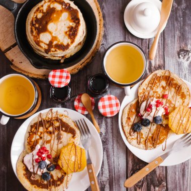 Reçel, kapaklar ve sawed ahşap sıcak tava ile çilek ile iki fincan çay, çatal, kaşık, dekore edilmiş krep ile iki beyaz plakaların üstten görünüm kavanozlar