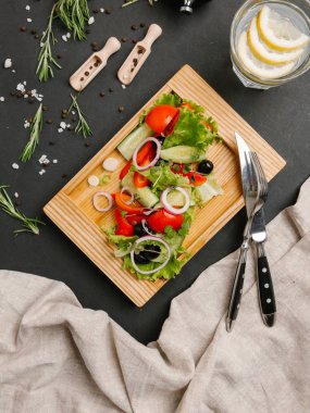 Taze dilimlenmiş salatalık, domates, tatlı soğan, zeytin, marul salatası ahşap tabak çatal, bıçak ve limonata ile hizmet 