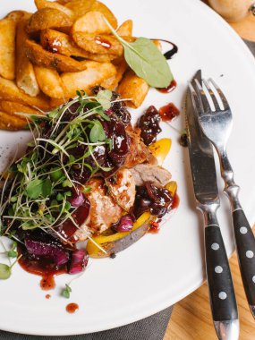 Kavrulmuş et ile tatlı soğan, kabak, berry soslu karamelize ve bezelye lahanası beyaz tabakta peçete, çatal, bıçak ve karabiber değirmeni ile derin kızarmış patates ile