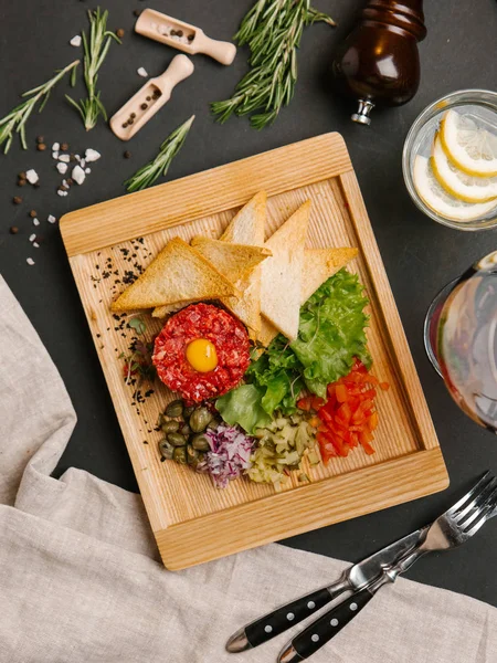 «Ana sayfa» görünümü sığır eti tartare ile Bıldırcın yumurta, ekmek tost, doğranmış turşu, tatlı soğan, domates, marul ve kapari servis ahşap tabak üzerinde bıçak, çatal, şarap ve limonata ile