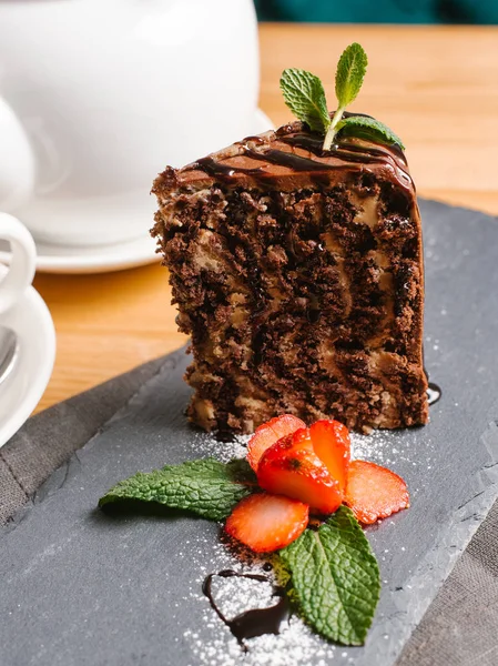 Chocolate zebra cake served on stone plate with sliced strawberry, mint leaves, powdered sugar, cup of tea and teapot