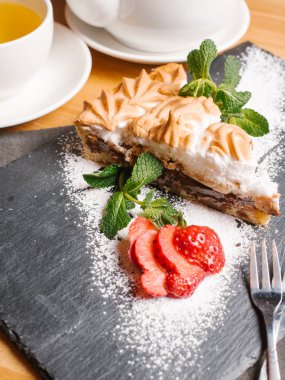 Pasta Bisküvi, meringues ve krem çikolata nane yaprakları ile taş tabakta servis, dilimlenmiş çilek, toz şeker, çatal ve çay seti