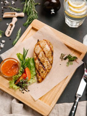 Izgara tavuk göğsü parşömen kağıt ile marul, domates ve ketçap ahşap tabak çatal, bıçak, limonata ve şarap sos servis