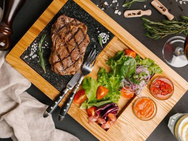 Üstten Görünüm taze domates, marul, tatlı soğan ile ızgara sığır eti biftek ketçap ve barbekü sosu, çatal, bıçak, limonata ve şarap ile ahşap yemek servis