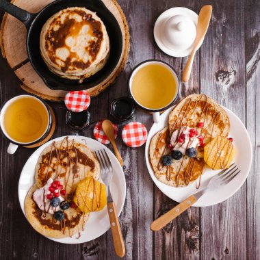 Reçel, kapaklar ve sawed ahşap sıcak tava ile çilek ile iki fincan çay, çatal, kaşık, dekore edilmiş krep ile iki beyaz plakaların üstten görünüm kavanozlar