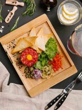 «Ana sayfa» görünümü sığır eti tartare ile Bıldırcın yumurta, ekmek tost, doğranmış turşu, tatlı soğan, domates, marul ve kapari servis ahşap tabak üzerinde bıçak, çatal, şarap ve limonata ile