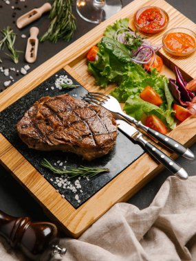 Ketçap ve barbekü sosu, çatal, bıçak ve peçete ile ahşap yemek iştah açıcı ızgara dana biftek taze domates, marul, tatlı soğan ile servis
