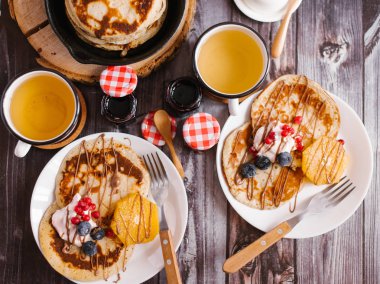 Reçel, kapaklar ve sawed ahşap sıcak tava ile çilek ile iki fincan çay, çatal, kaşık, dekore edilmiş krep ile iki beyaz plakaların üstten görünüm kavanozlar