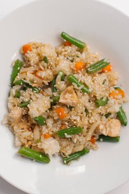 Risotto ile kavrulmuş tavuk parçaları, havuç, lahana ve Fransızca fasulye beyaz tabakta susam ile dekore edilmiş kapatmak