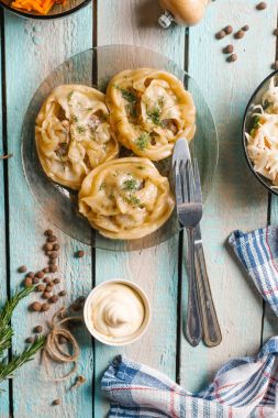 Üstten Görünüm mantı, bıçak, çatal, ekşi krema, öğütücüler ve dilimlenmiş havuç ile cam tabak mavi ahşap masa üzerinde servis