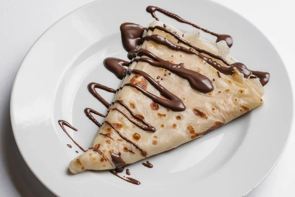 Closeup of crepe with chocolate syrup served on white plate isolated on white background
