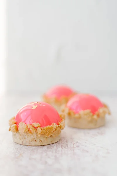 Food composition of three glazed pink cakes served on marble surface with blurred background