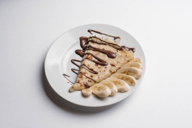 Çikolata şurubu ve dilimlenmiş muz krep izole beyaz arka plan üzerinde beyaz tabakta servis