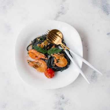 Karides, domates ve yeşillik çatal ve kaşık beyaz plaka üzerinde siyah makarna