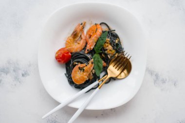 Karides, domates ve yeşillik çatal ve kaşık beyaz plaka üzerinde siyah makarna