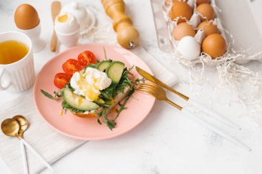 Dilimlenmiş avokado, kiraz domates, roka çatal bıçak takımı, yumurta ve çay Kupası ile pembe plaka üzerinde Gıda kompozisyonu