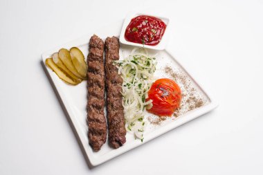 Beyaz tabakta kebap dilimlenmiş sebzeler ve ketçap