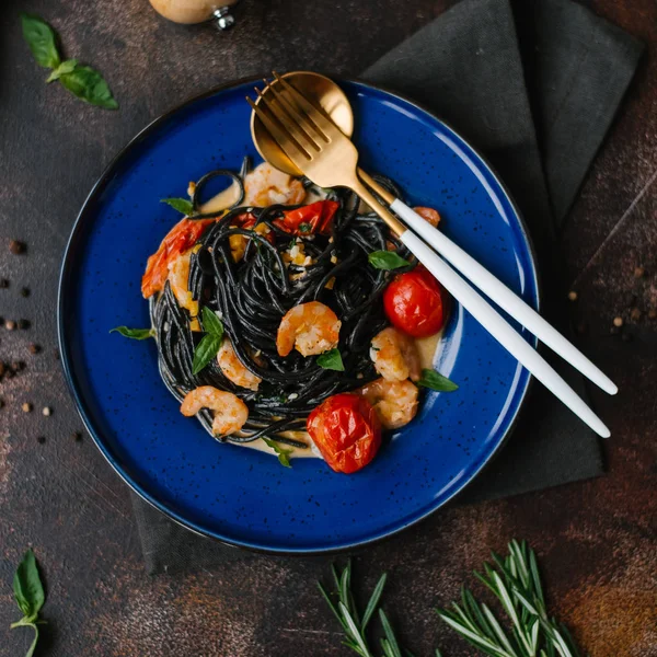 トマト フォーク スプーン 青い皿の上の緑と黒のパスタのクローズ アップ ペッパー グラインダーとテーブルの上のハーブ — ストック写真