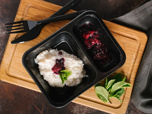 Risotto with wild berries served on black plate with knife and fork