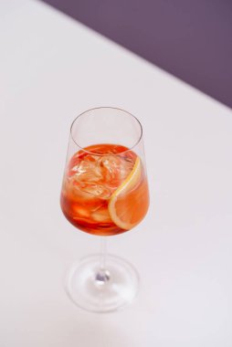 glass of aperol spritz cocktail with ice and orange on white table 