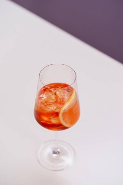 glass of aperol spritz cocktail with ice and orange on white table 